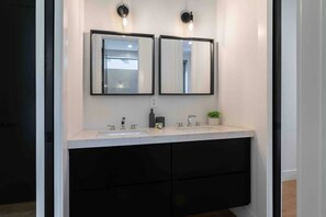 Un baño moderno con lavamanos doble, dos espejos montados en la pared y un gabinete negro debajo.