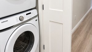 Un área de lavandería con dos lavadoras Samsung blancas, una puerta cerrada y piso de madera.