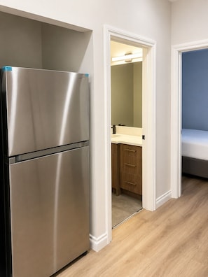 A compact kitchen with a stainless steel refrigerator, a wooden cabinet, and a small countertop. - Calgary Urban Suites B (Calgary)