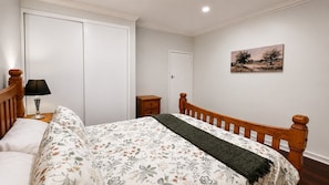 A bedroom with a bed, a nightstand, a lamp, a wardrobe, and a painting on the wall.