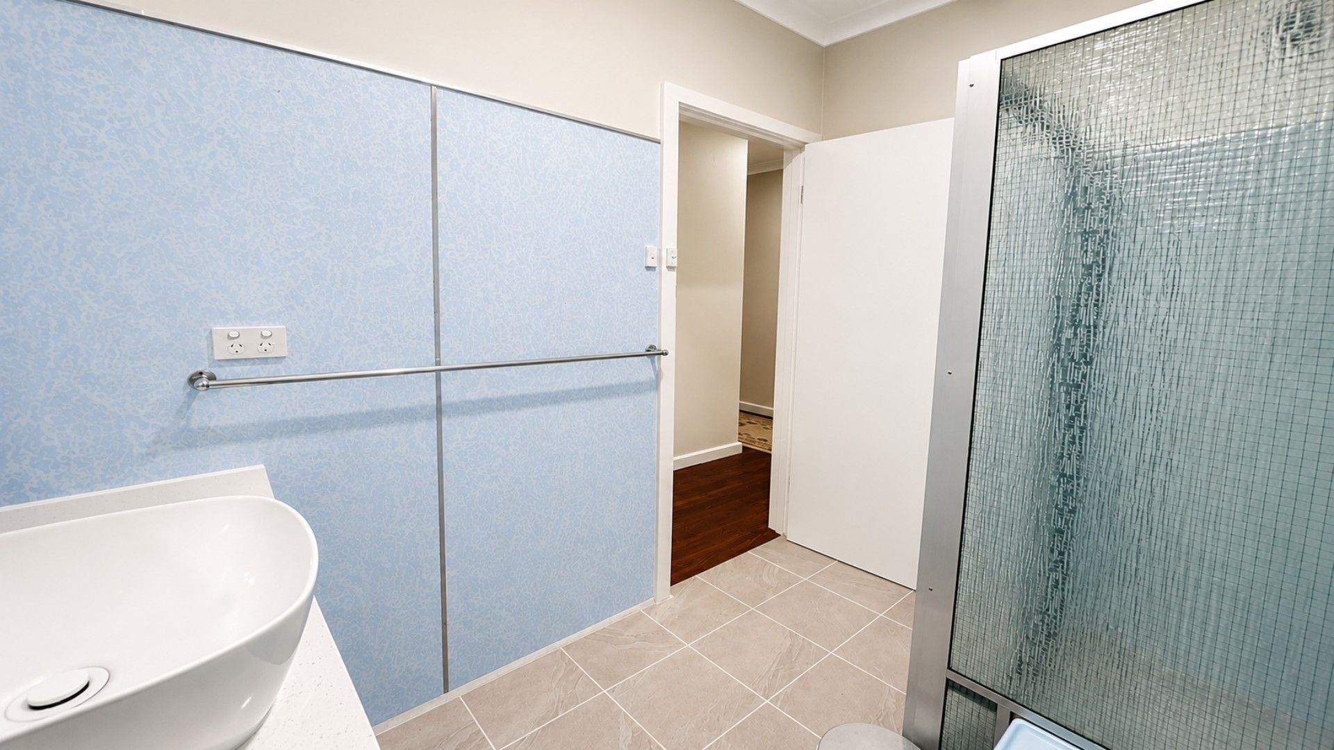 A bathroom with a white sink, a glass shower enclosure, and a blue wall.