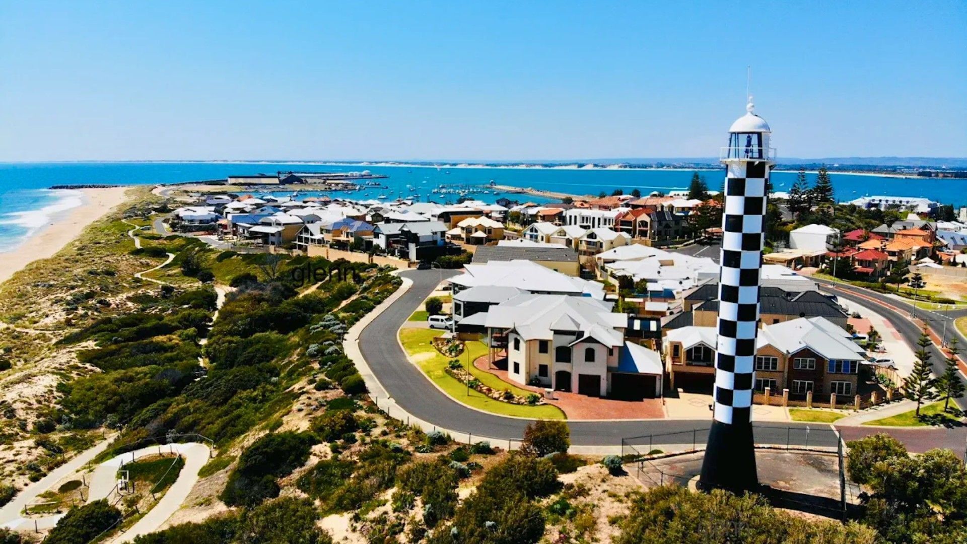 Un pueblo costero con un faro destacado, edificios residenciales y una playa.