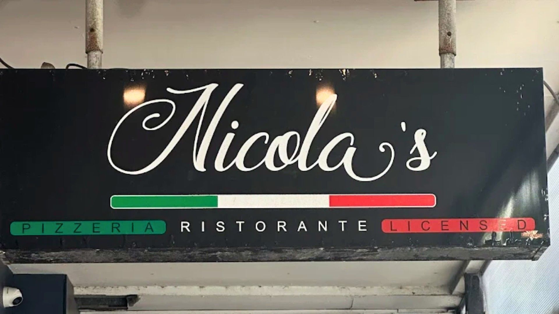 Een bord voor 'Nicola's' met de woorden 'PIZZERIA', 'RISTORANTE' en 'LICENTIE'.
