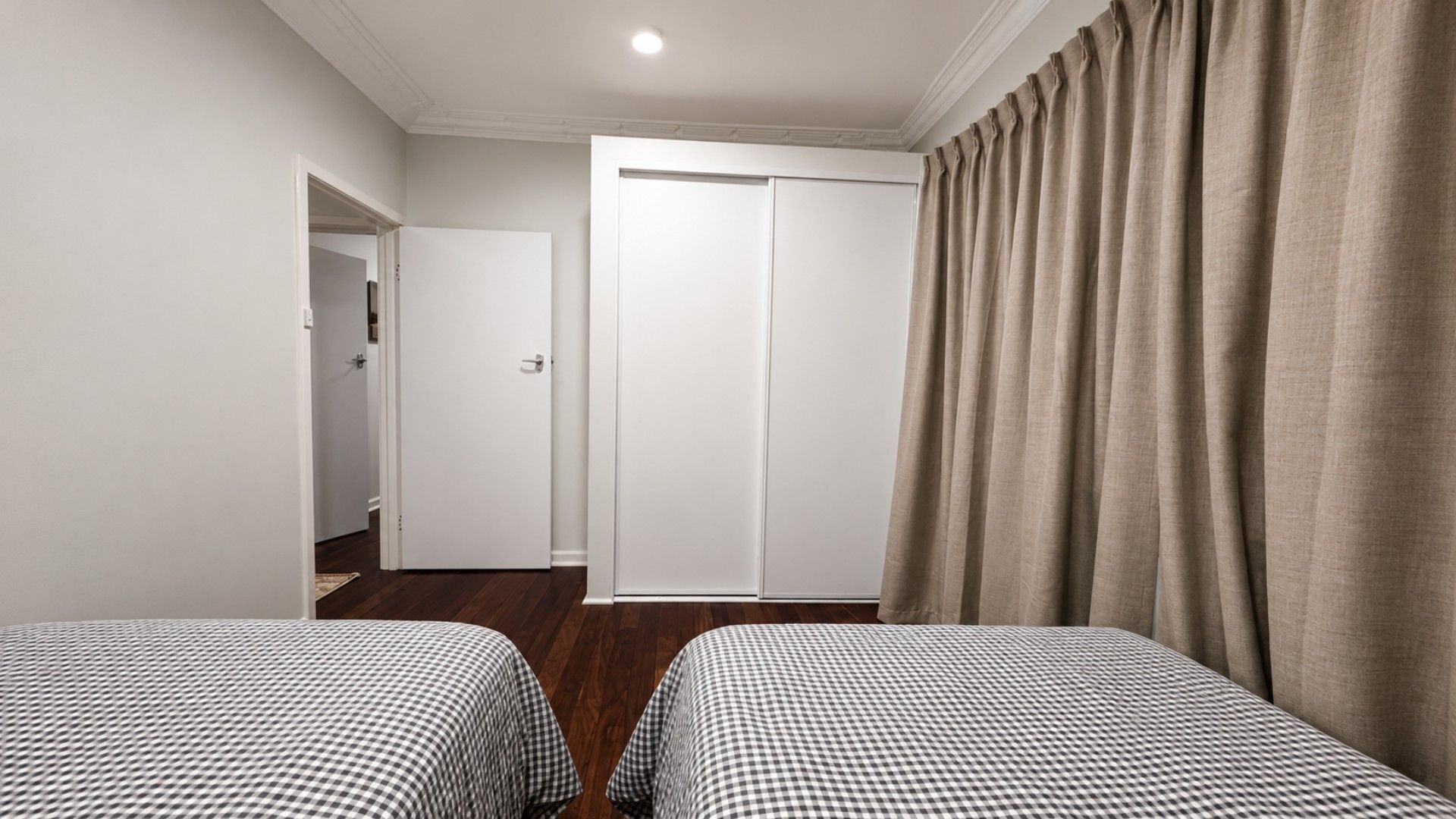 A hotel room with two single beds, a wardrobe, a door, and a curtain.
