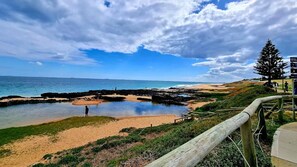 Une plage côtière bordée de formations rocheuses, avec une promenade en bois et une vue dégagée sur l’océan.