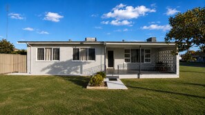 Une maison de plain-pied avec un porche à l’avant, un petit jardin et un ciel d’un bleu éclatant.