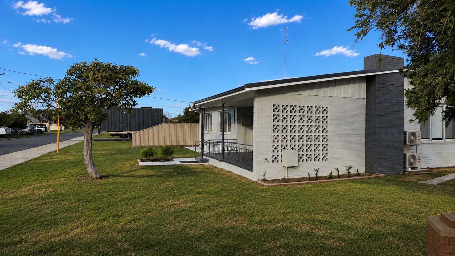 A modern single-story house with a covered porch, a small garden, and a clear blue sky.