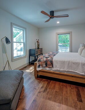 Ein Schlafzimmer mit Bett, Schreibtisch, Stuhl, Stehlampe und zwei Fenstern.