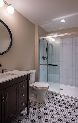 Un bagno con WC, lavandino, specchio, cabina doccia e pavimento decorato.