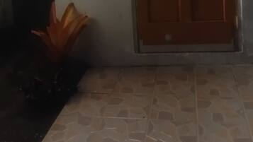 Een gebouwde ingang met een houten deur, een lamp boven de deur en een betegelde vloer.