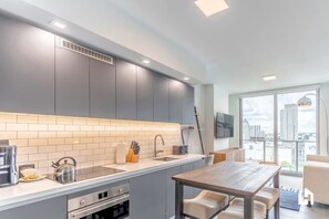 Eine moderne Küche mit grauen Schränken, einer weißen Arbeitsplatte und einem Essbereich mit Holztisch und Stühlen.