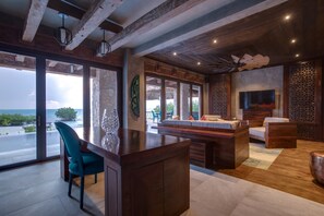 A modern interior with a wooden ceiling, a stone accent wall, a large window with a view of the sea, and a seating area with a TV.