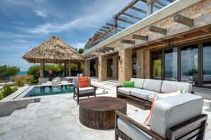 A modern outdoor living area with a pool, seating, and a view of the ocean.