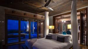 Un dormitorio con una cama grande, un ventilador de techo y vistas a través de una puerta de cristal.