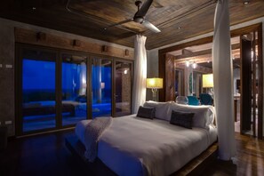 Un dormitorio con una cama grande, un ventilador de techo y vistas a través de una puerta de cristal.