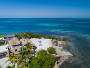 A beachside property with a thatched-roof hut, lounge chairs, and a clear view of the turquoise sea. - Gladden Private Island (Placencia)