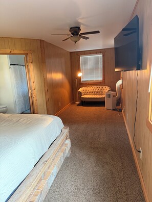 A bedroom with a bed, a ceiling fan, a window with blinds, a television, and an air conditioning unit. - Cozy 2-bedroom lake view house in charming Poynette with AC (Poynette)