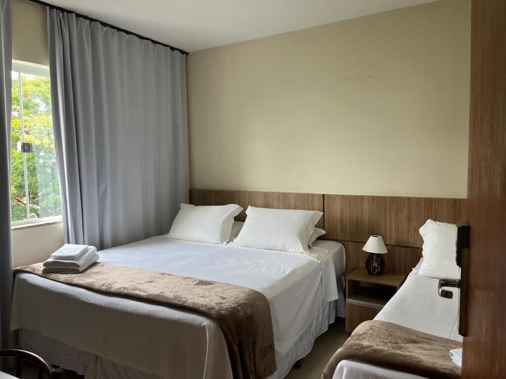 A hotel room with a bed, a nightstand, a lamp, and a window with curtains.