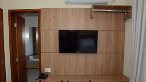A room with a wooden desk, a flat-screen TV mounted on the wall, a chair, and a small white cabinet.