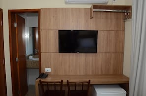Ett rum med ett skrivbord i trä, en platt-TV som är monterad på väggen, en stol och ett litet vitt skåp.