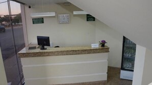 A reception desk with a clock, a small plant, and a refrigerator.