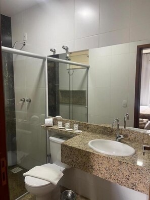 A bathroom with a glass shower enclosure, a sink with a granite countertop, and a toilet. - Hotel Monte Carlo (são joão del rei)