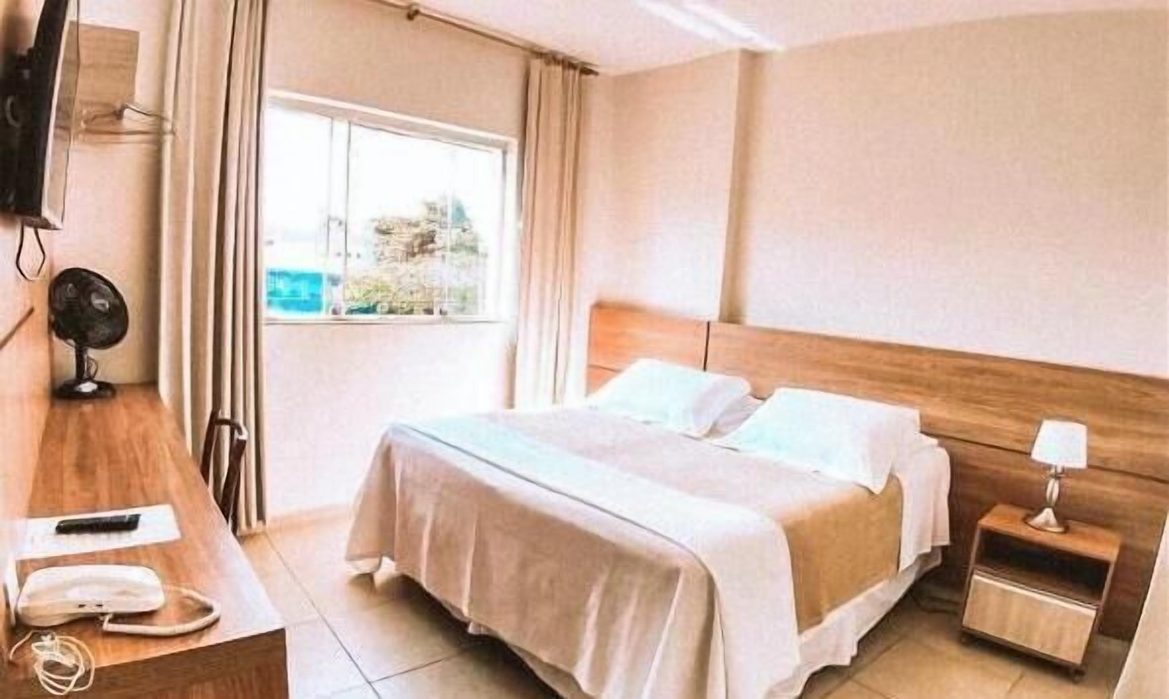 A hotel room with a bed, bedside table, lamp, and a window with curtains.