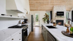Een moderne keuken met een stenen openhaard, een houten plafond en een groot raam met uitzicht op een tuin.
