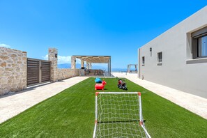Ein Garten mit einem Fußballtor, einer Steinmauer, einer überdachten Sitzgelegenheit und einem Motorrad.