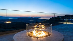 Een vuurkuil met een glazen omheining op een balkon met uitzicht op verre bergen.