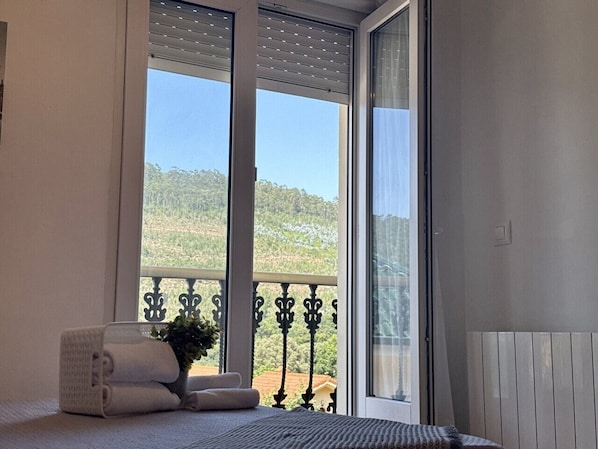 A room with a bed, a window with a view of a hill, and a balcony with a railing. - Amarena Apartment 20812 (Argoños)