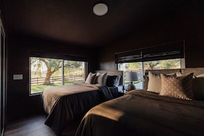 Ein Schlafzimmer mit zwei Betten, einem Nachttisch, einer Lampe und Blick auf einen Baum.