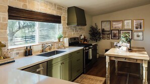 Une cuisine avec un mur en pierre, une fenêtre donnant sur un beau paysage, une cuisinière et une table à manger avec un plateau.
