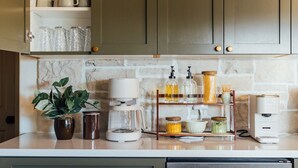Une cuisine avec un dosseret en marbre, une machine à café, des bocaux et une plante en pot.