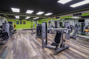 Ein Fitnessstudio mit verschiedenen Trainingsgeräten, grünen Wänden und Holzboden.