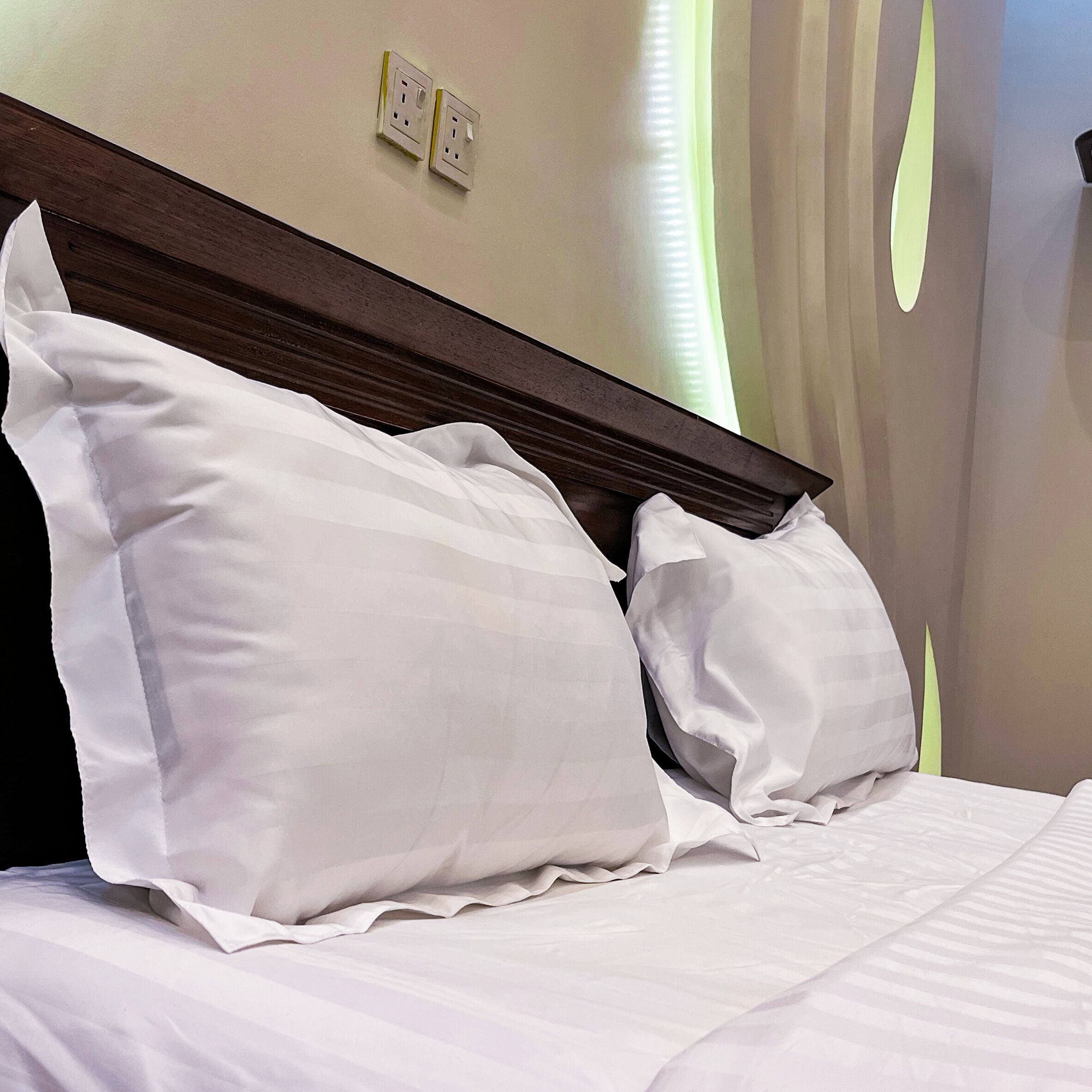Una cama bien hecha con ropa blanca y almohadas, un cabecero de madera y dos enchufes de pared.