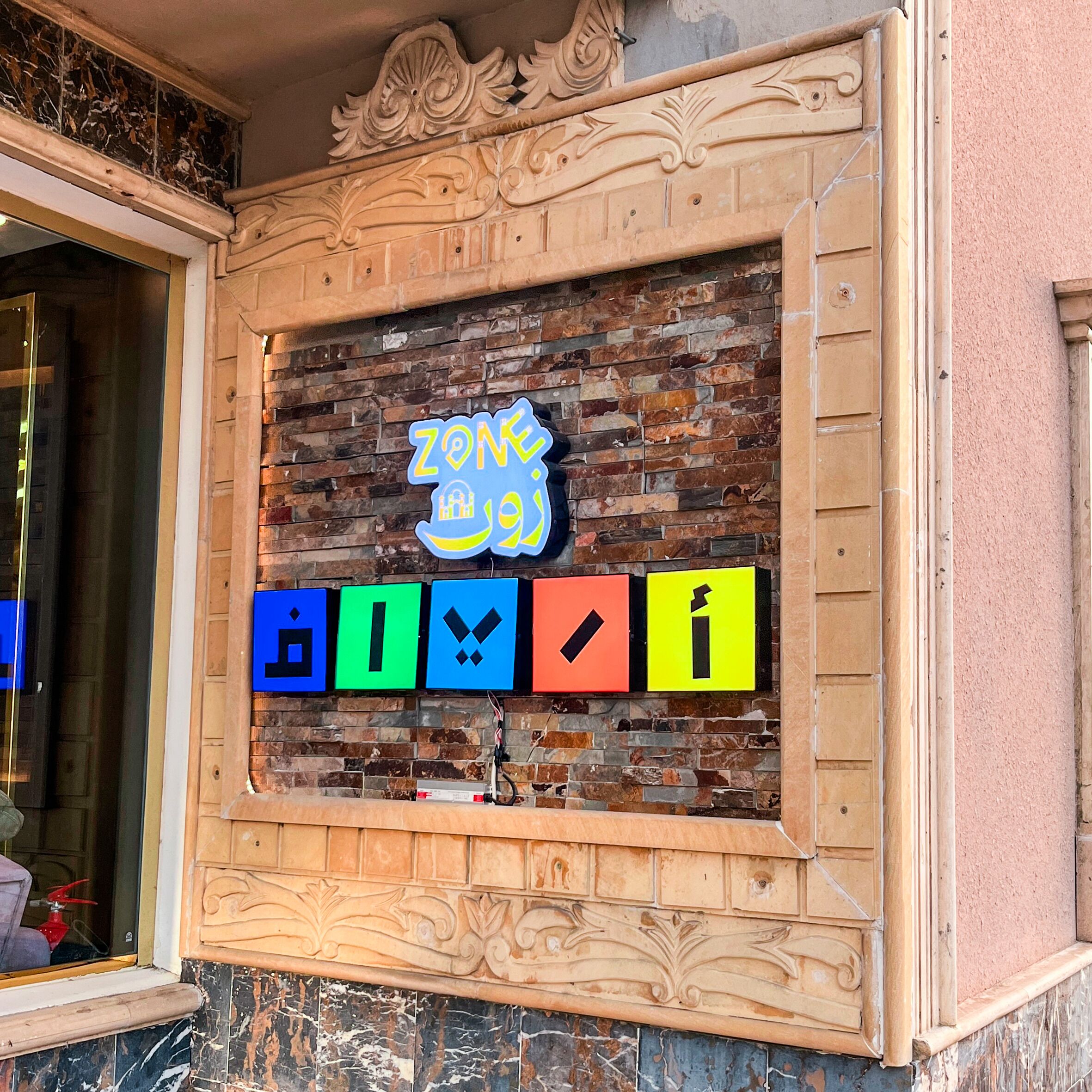 Un mur avec un motif en briques, un cadre en bois décoratif et une signalétique colorée ornée de symboles.