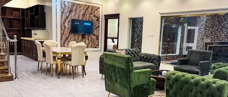 A modern living room with a dining area, a television mounted on a marble wall, and a staircase leading to another level.