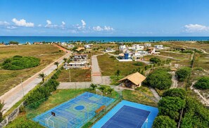 Vista aérea de uma área residencial com casas, quadra de basquete e uma praia ao fundo.