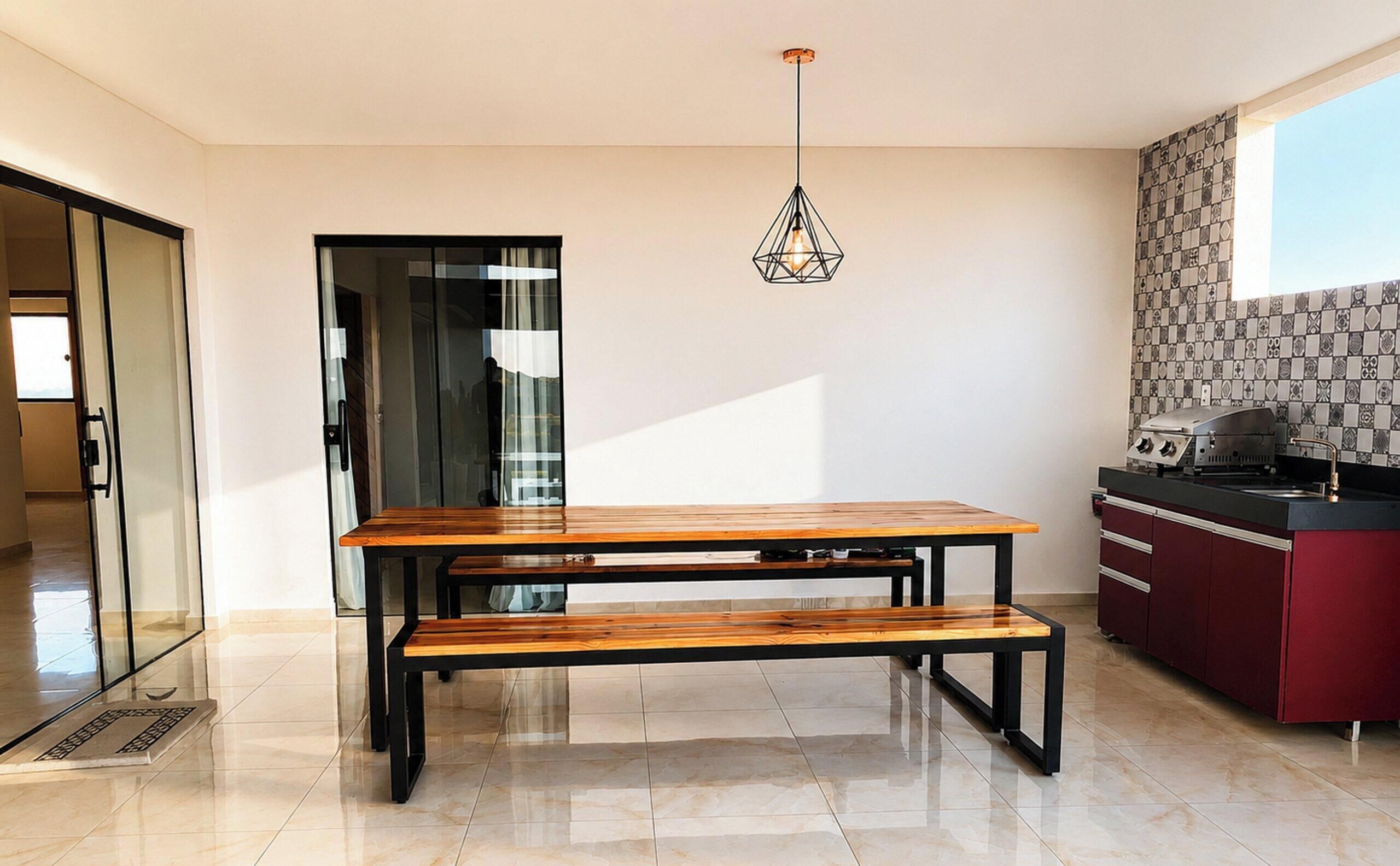 Une cuisine moderne avec une table et un banc en bois, un luminaire suspendu et un revêtement mural en carreaux.