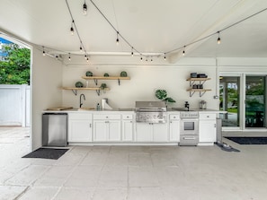 A modern kitchen with white cabinets, a stainless steel stove, and overhead string lights. - Heated Pool! Tropical Backyard! Hammock+Ping-Pong! (Oakland Park)