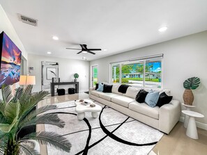 A modern living room with a white sofa, a coffee table, and a large TV. - Heated Pool! Tropical Backyard! Hammock+Ping-Pong! (Oakland Park)