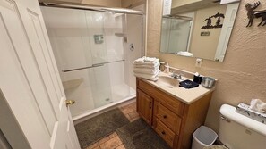 Et badeværelse med brusekabine i glas, et træbord med vask og et toilet.