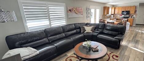 A living room with a black leather sectional sofa, a round coffee table, and a patterned rug.