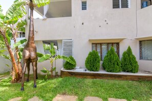 Ein Gebäude mit Flachdach, Balkon und kleinem Garten, inklusive Statue und geschnittenen Büschen.