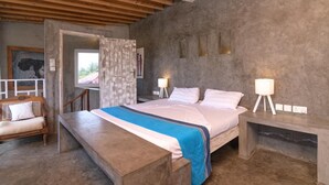 Ein Schlafzimmer mit einem Bett, Nachttischlampen, einer Holzbank, einem Deckenventilator und Blick durch eine offene Tür.