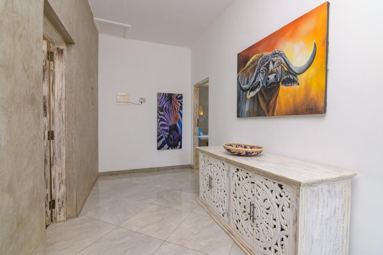 A hallway with a white wall, a decorative cabinet, and two paintings.