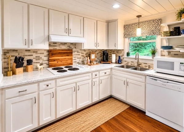 A modern kitchen with white cabinetry, a tiled backsplash, a built-in stove, a microwave, and a window with a view of greenery. - Guthrie Ridge-Charming Getaway, Gorgeous Views! (Waynesville)