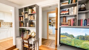 Una cuina moderna amb armaris blancs, una zona de menjador amb taula i cadires de fusta, i una prestatgeria plena de llibres i elements decoratius.
