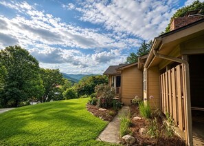 A house with a well-maintained lawn, a pathway leading to the entrance, and a view of the surrounding landscape. - Guthrie Ridge-Charming Getaway, Gorgeous Views! (Waynesville)